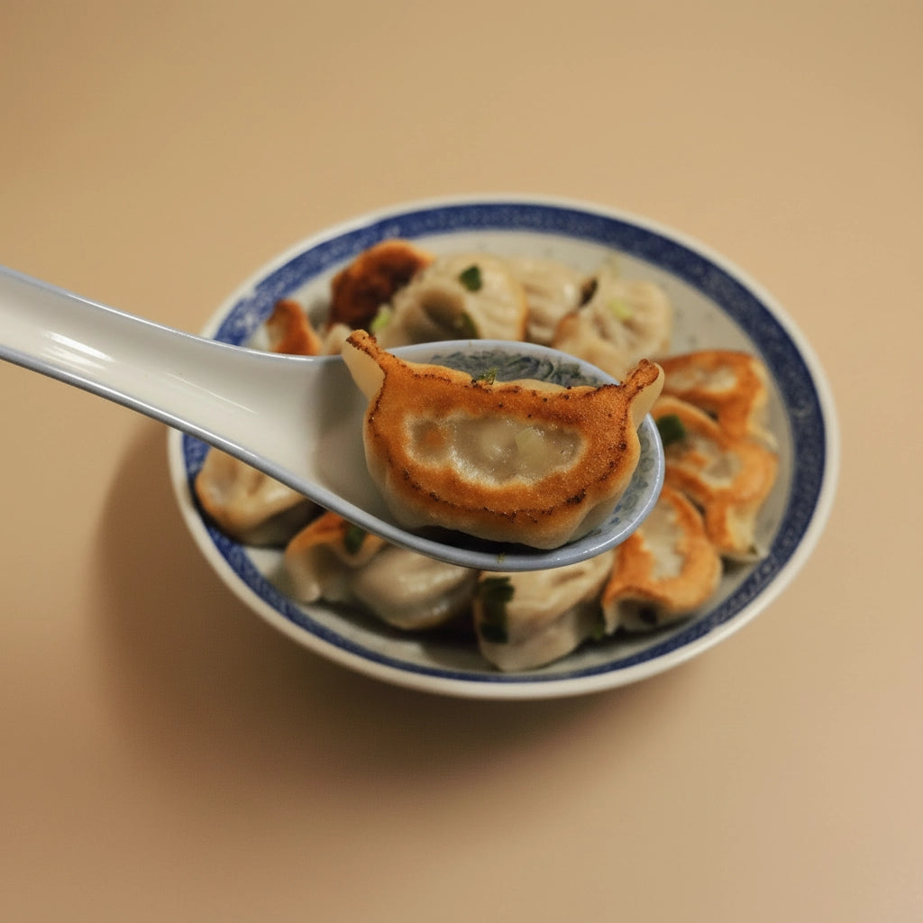 Pan fried dumplings on a spoon with a plate of more dumplings on a beige background.