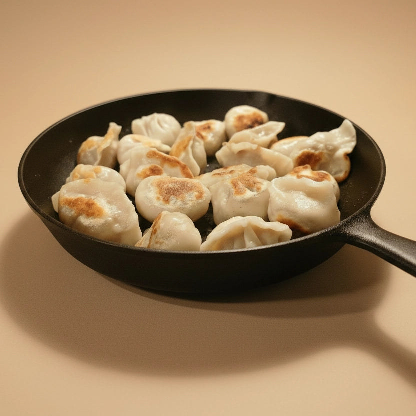 Dumplings cooking in a black frying pan on a beige background